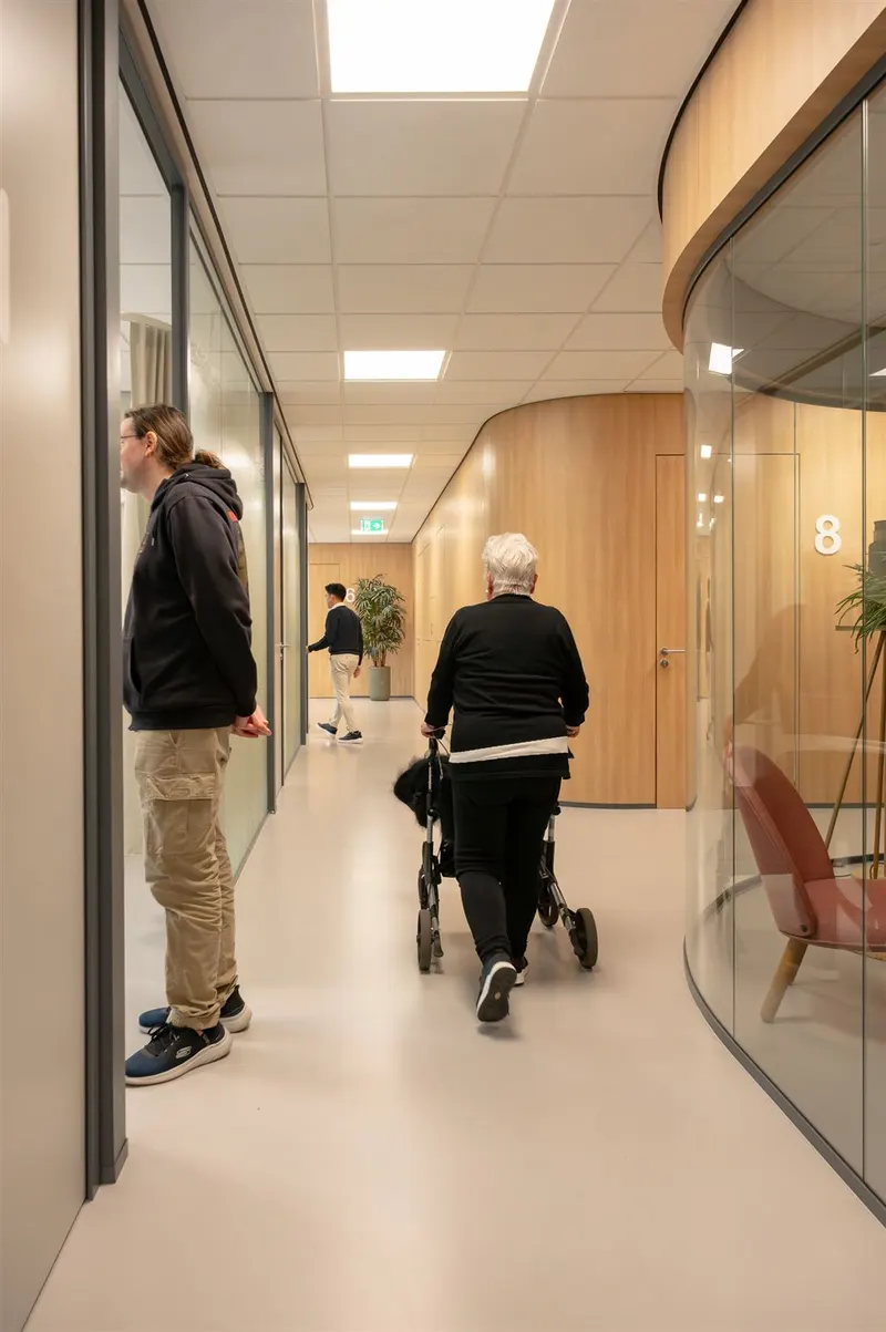 Oudere patiënt met rollator in de gang van de praktijk